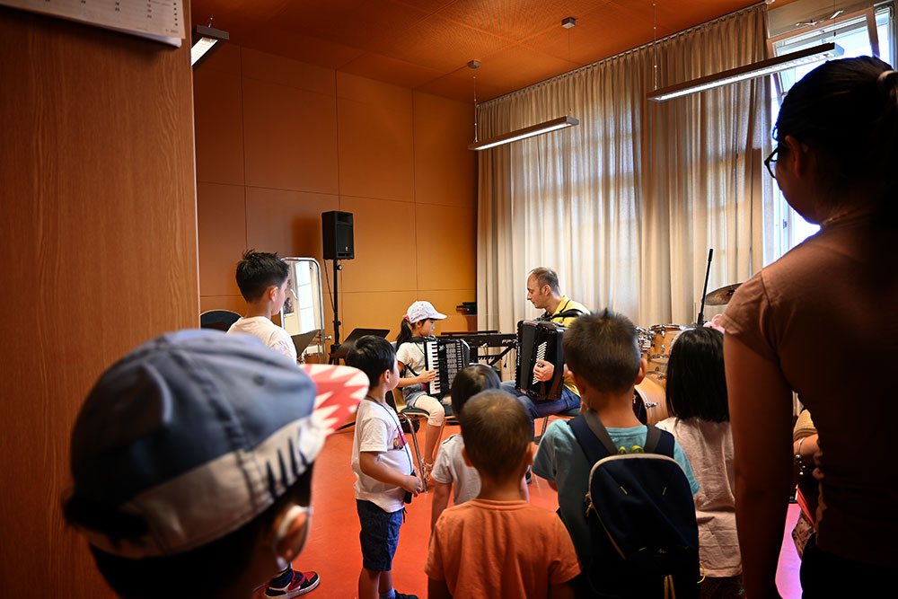 Viele Kinder stehen im Raum mit den Akkordeons. im Hintergrund Lehrer und Schüler mit je einem Akkordeon.