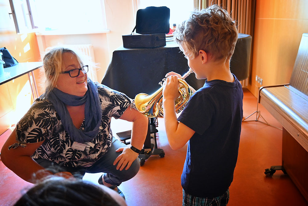 Ein kleiner Junge spielt auf der Trompete, die Trompetenlehrerin schaut zu.