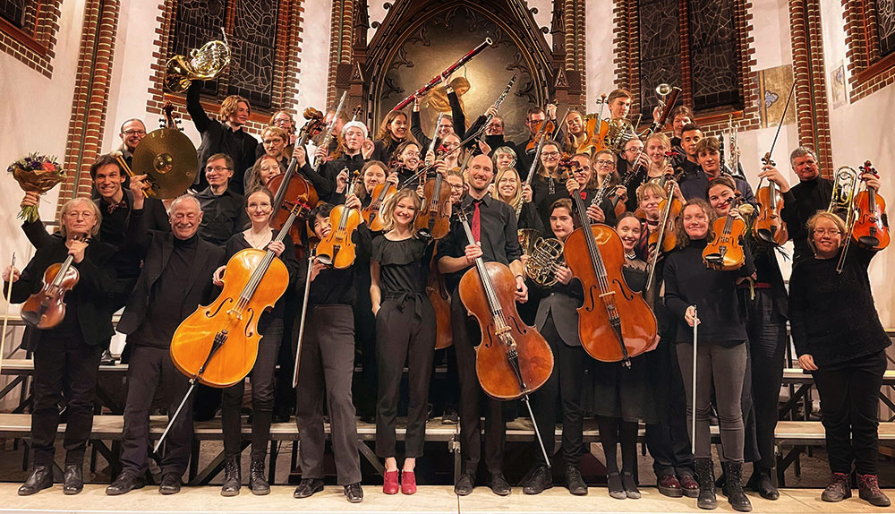 Das Schostakowitsch-Sinfonieorchester steht vor dem Altar der Erlöserkirche. Alle halten ihre Instrumente hoch.