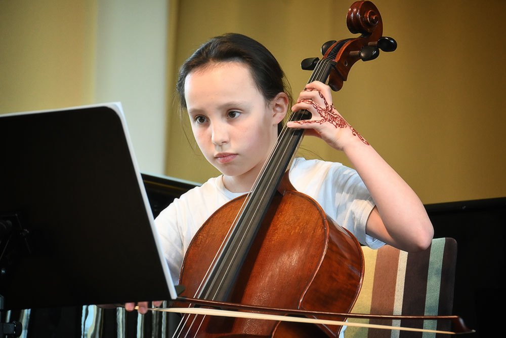 Ein Mädchen spielt ihr Cello und blickt dabei in ihre Noten, die auf einem Pult stehen