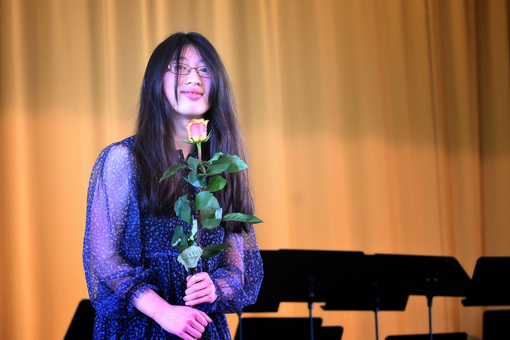 Die Pianistin in einem blauen Kleid auf der Bühne mit einer Rose in den Händen